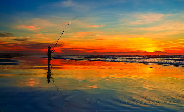 A fisherman at sunset on a highly reflective beach a man when fishing on a beach at sunset sea fishing stock pictures, royalty-free photos & images