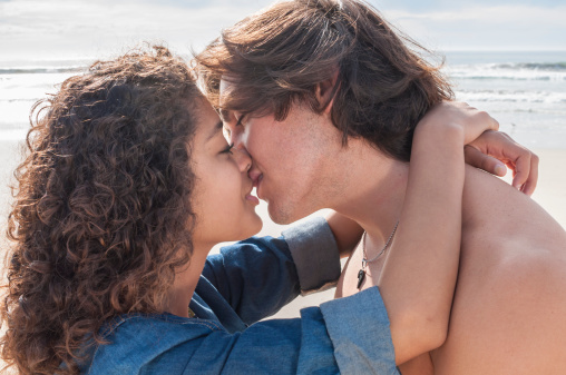 Closeup of happily in love young man and woman embracing and kissing while alone on a beautiful beach