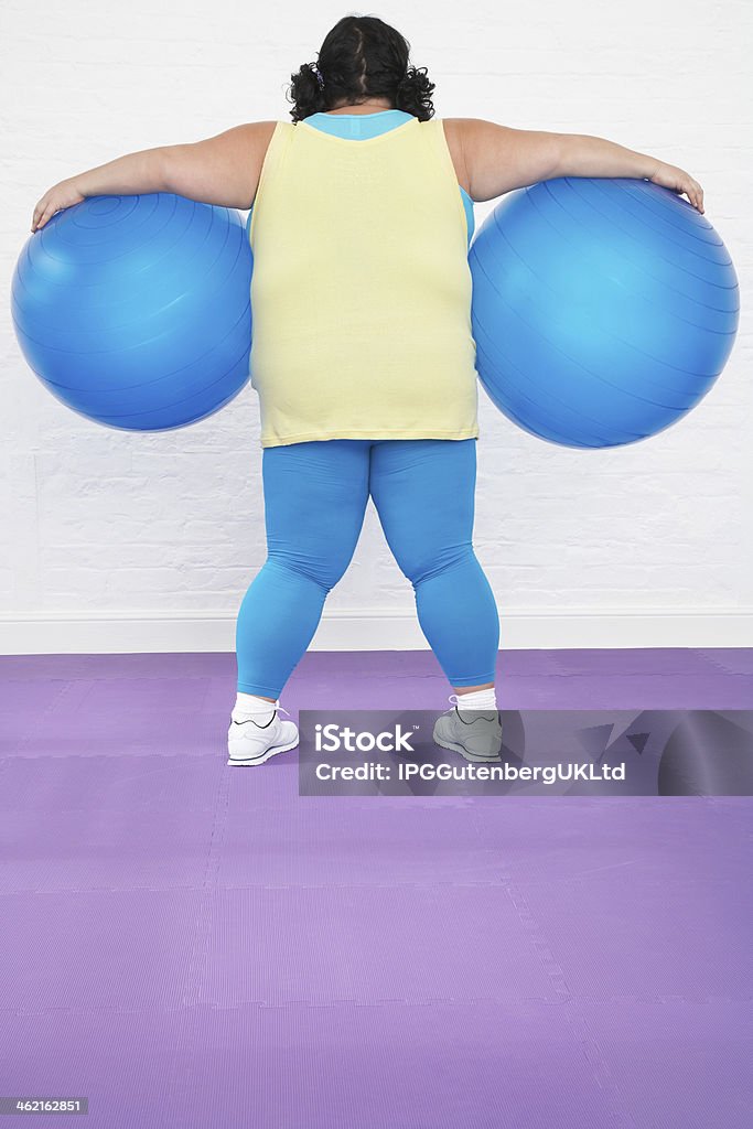 Overweight Woman Holding Two Exercise Balls Rear view of an overweight woman holding two exercise balls in healthclub Adult Stock Photo