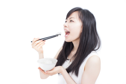 Beautiful young girl eating rice with chopsticks, isolated on white background.