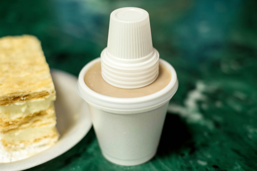 A white cup containing Cuban Coffee (Colada) with the thimble sized dispensing cups.  In the background is typical Cuban dessert with white cream filling.