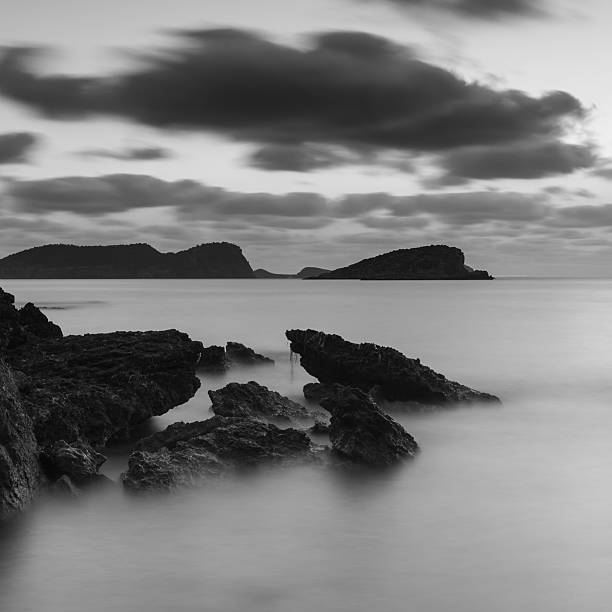 восход солнца над скалистыми береговая линия в черно-белом - black and white landscape square long exposure стоковые фото и изображения