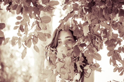 vintage like portrait of a female teenager behind some leafs.