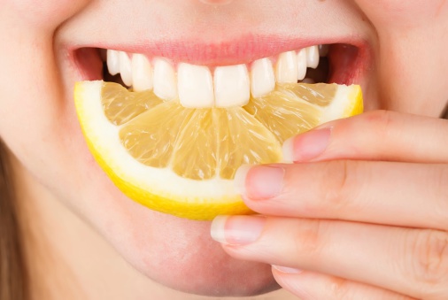 Close-up of a woman tasting sour lemon and smiling.