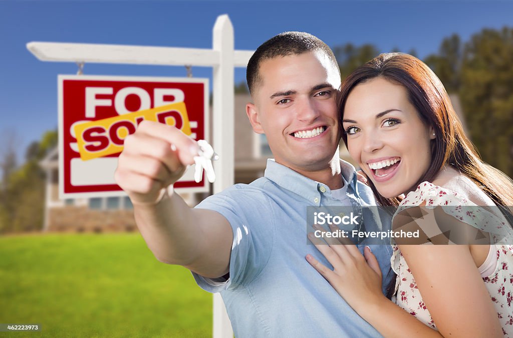 Military Couple In Front of Home, House Keys and Sign Mixed Race Excited Military Couple In Front of New Home with New House Keys and Sold Real Estate Sign Outside. Adult Stock Photo