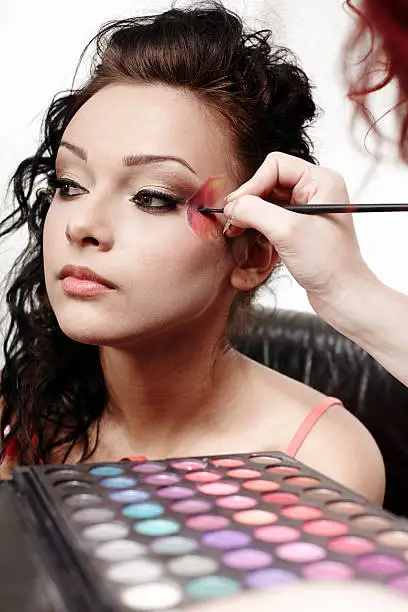 Portrait of a beautiful woman having makeup applied by makeup artist