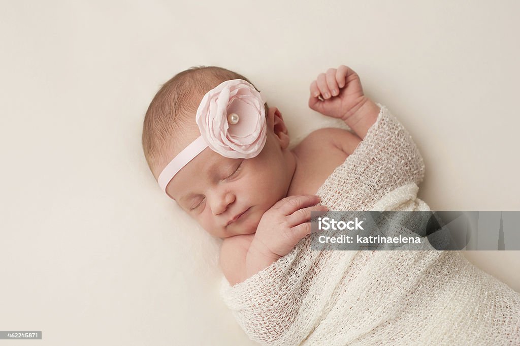 Newborn Baby Girl with Light Pink Flower Headband A portrait of a beautiful, 12 day old newborn baby girl wearing a light pink flower headband. She is swaddled and sleeping on her back on a cream colored blanket. Baby Girls Stock Photo