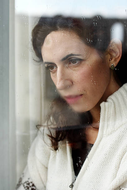 istock Woman with sad expression looking out of a window 462264993