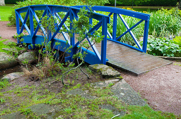 Blue small bridge over river stream creek in green garden. Nature and landscape.