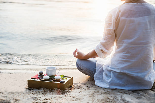 Woman meditating with tea and stones on a beach shore stock photo