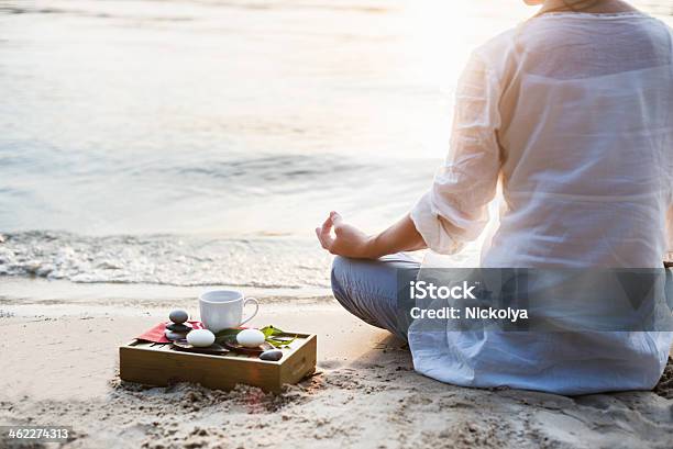 Woman Meditating With Tea And Stones On A Beach Shore Stock Photo - Download Image Now