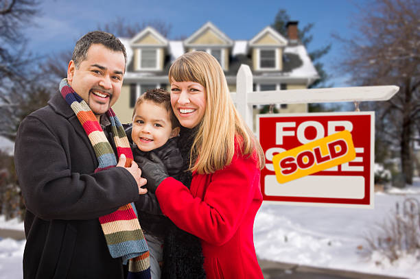 Family in Front of Sold Real Estate Sign and House Warmly Dressed Young Mixed Race Family in Front of Sold Home For Sale Real Estate Sign and House with Snow On The Ground. for sale sign photos stock pictures, royalty-free photos & images
