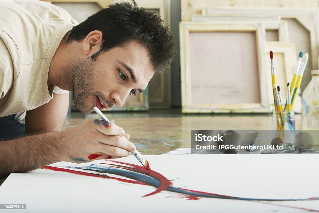 Man Painting On Canvas Studio Floor Closeup of a young man painting on canvas on studio floor Adult Stock Photo