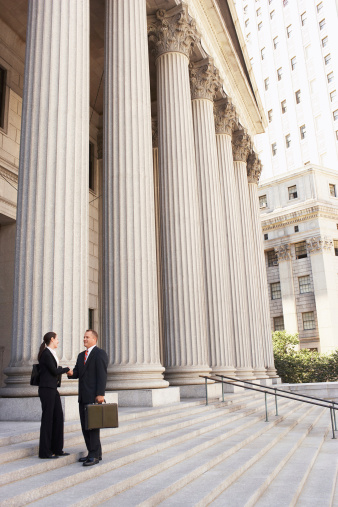 Full length side view of male and female attorneys shaking hands on courthouse steps