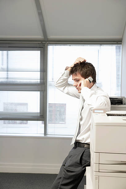 istock Uncertain Businessman By Photocopier Using Cellphone 462313347