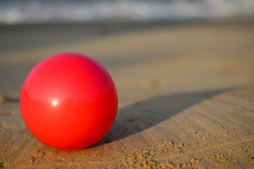 Red beachball on sand near the sea
