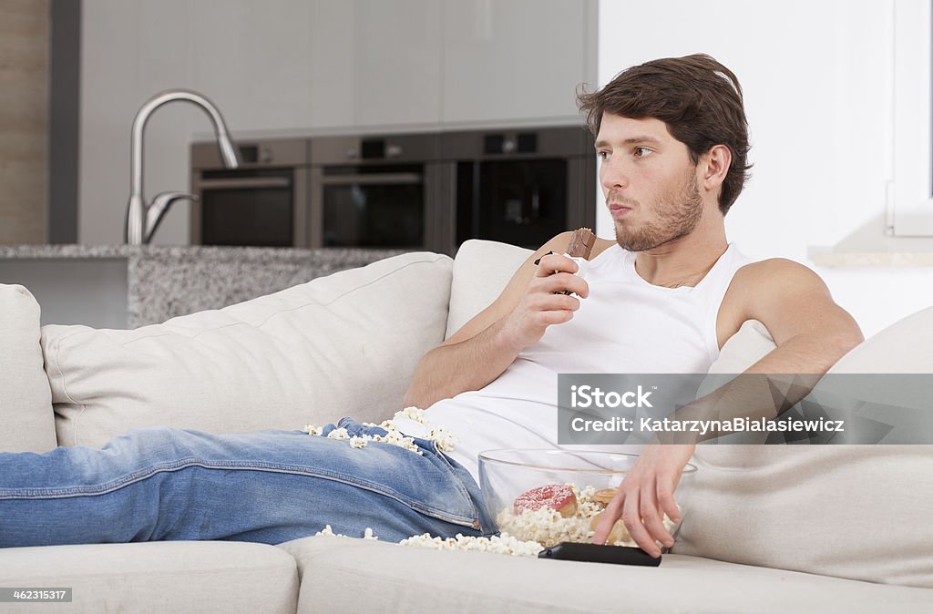 Bored man lying on couch Bored man lying on couch and eating sweets Eating Stock Photo