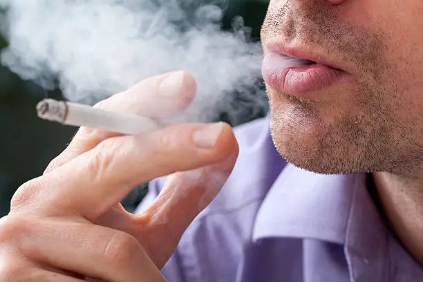 A closeup of a man breathing out the cigarettes' smoke