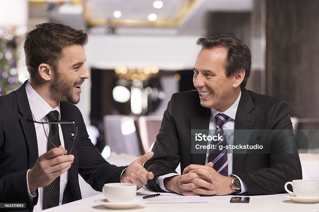 Great success. Two cheerful business people in formalwear discussing something and smiling while sitting at the restaurant Adult Stock Photo