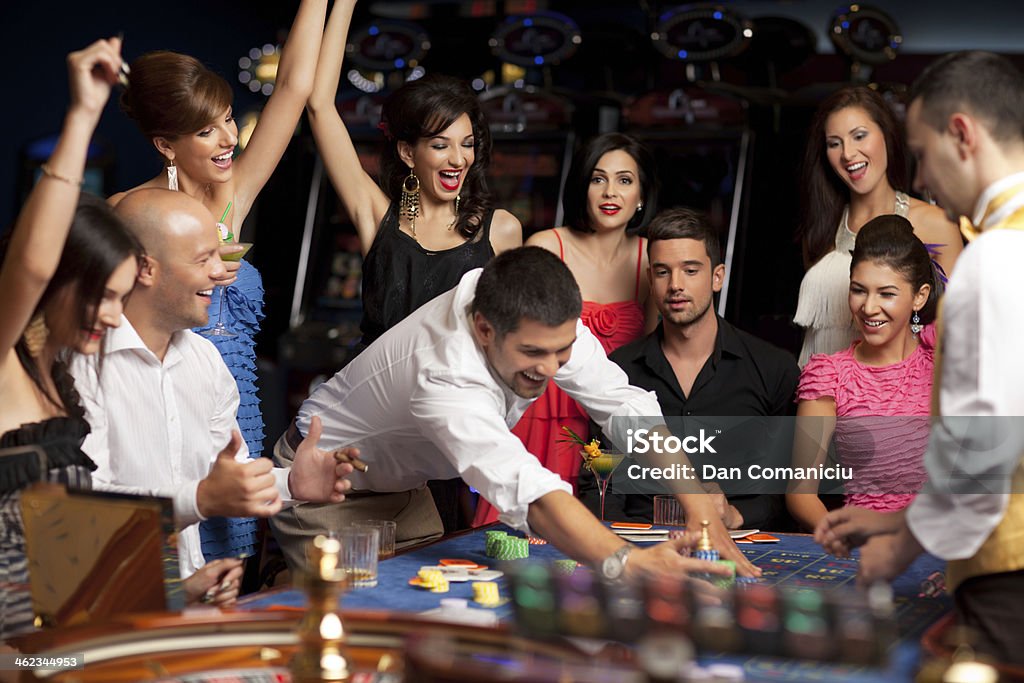 happy caucasian friends playing roulette in casino adult group celebrating friend winning at roulette Adult Stock Photo