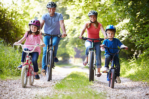vierköpfige familie reiten fahrräder auf kies road - radfahren stock-fotos und bilder