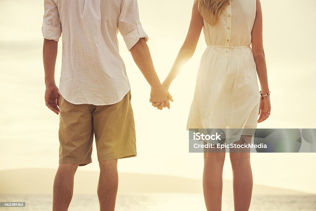 Young couple in love on the beach sunset Young couple in love, Attractive man and woman enjoying romantic evening on the beach, Holding hands watching the sunset Walking Stock Photo