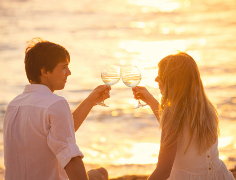 Honeymoon concept, Man and Woman in love, Couple enjoying glass of champagne on tropical beach at sunset, Beautiful sunset light