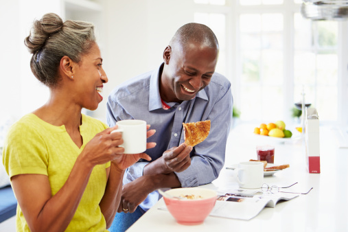 African American Couple Having Breakfast And Reading Magazine In Kitchen