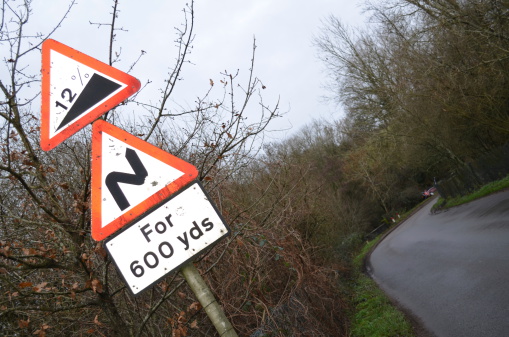 Traffic signs warning road users of dangerous road conditions. A car is in the shot which has skidded and crashed into the ditch on the bend.