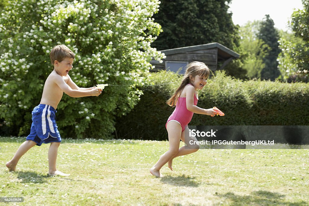 Boy Shooting Girl With Water Pistol In Backyard Full length side view of a boy shooting girl with water pistol in the backyard Boys Stock Photo