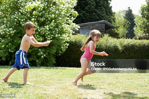 Boy Shooting Girl With Water Pistol In Backyard Stock Photo - Download Image Now - Boys, Carefree, Cheerful
