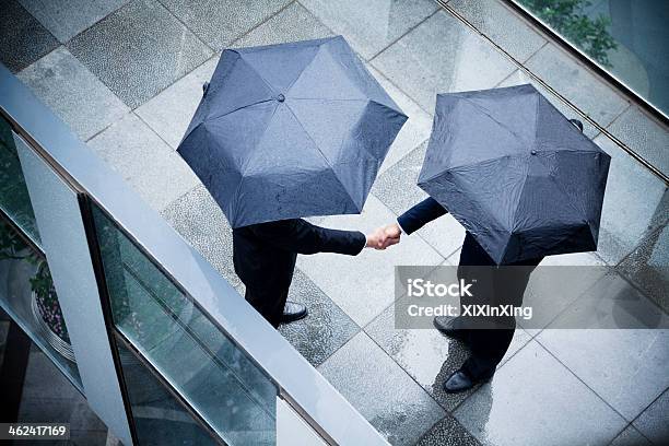 Dos Hombres De Negocios Estrechándose Las Manos Sosteniendo Sombrillas Y En La Lluvia Foto de stock y más banco de imágenes de Paraguas