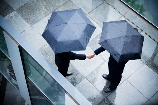 High angle view of two businessmen holding umbrellas and shaking hands in the rain