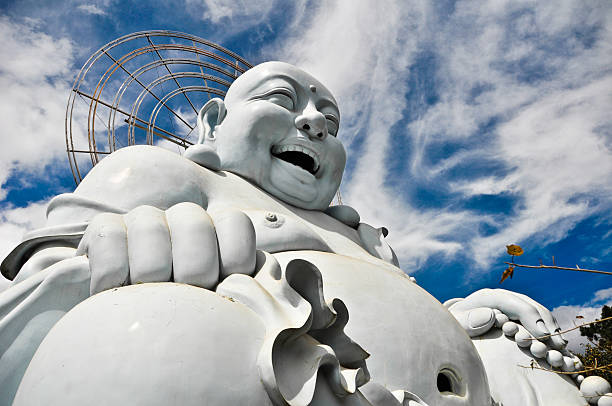 Cheerful statue of Laughing Buddha holding an offering bowl, symbolizing prosperity and happiness, set against a stone wall background.
