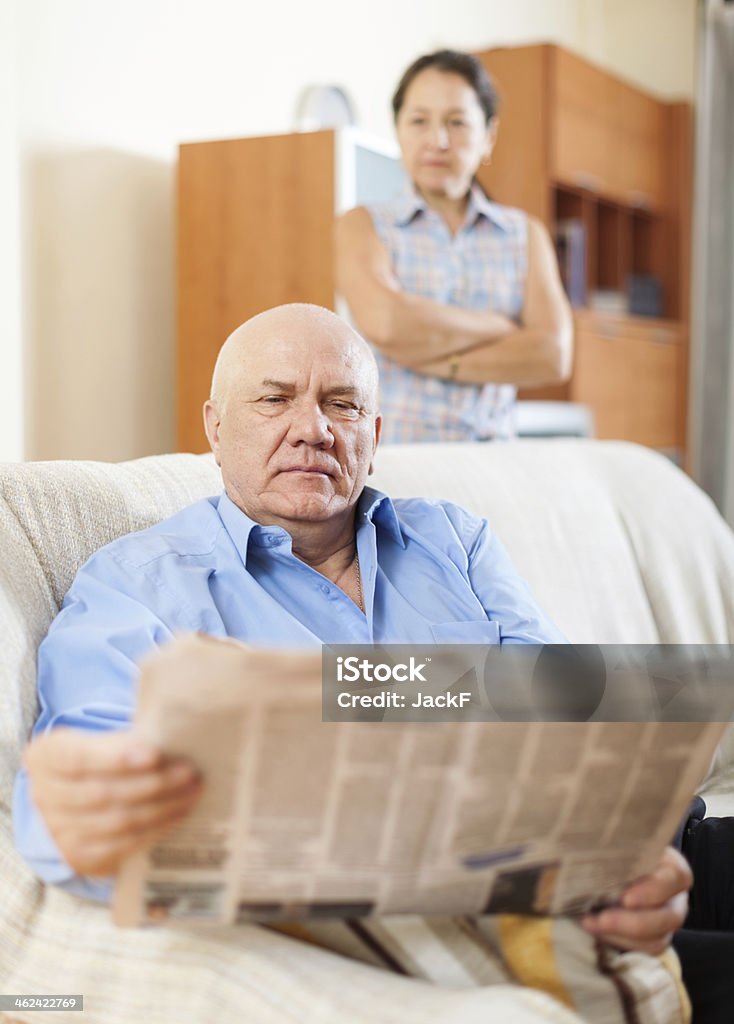 mature man reading newspaper against sad woman serious mature man reading newspaper against sad woman in home 50-59 Years Stock Photo