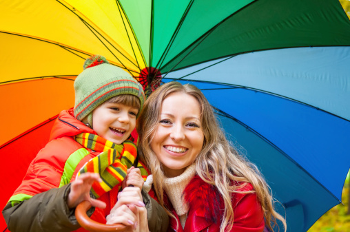 Happy family with bright multicolored umbrella in autumn park