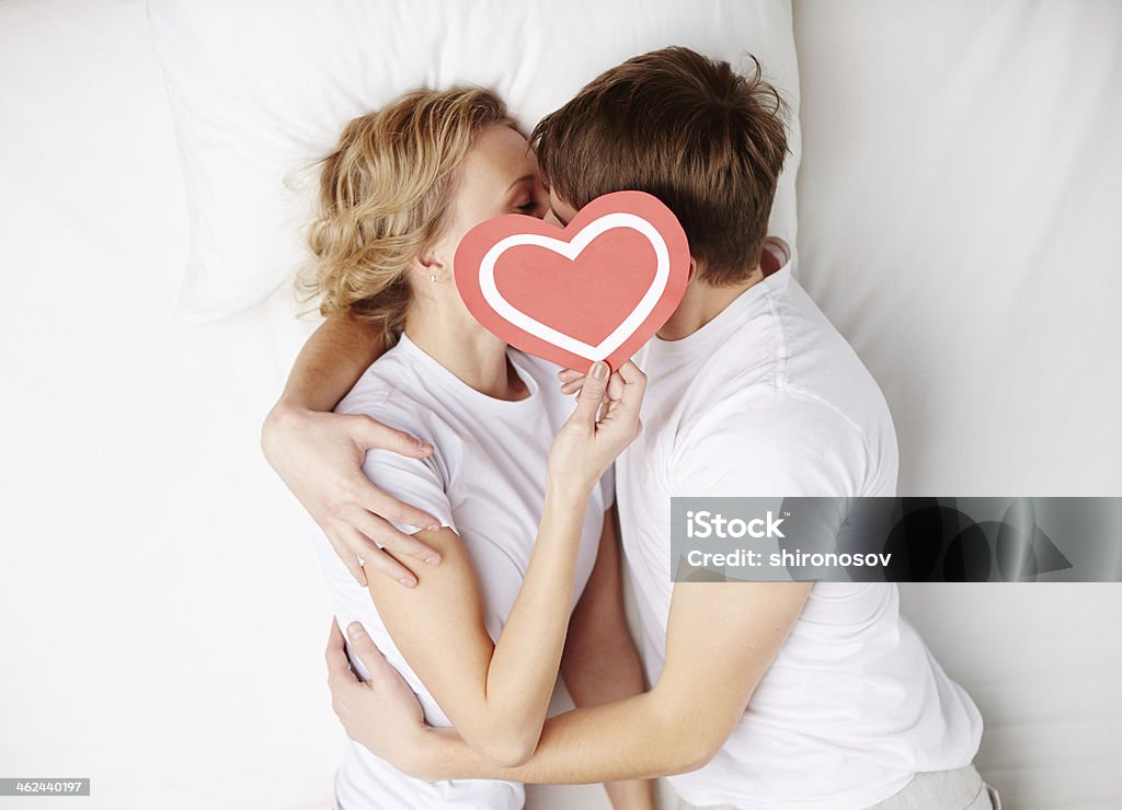 Sweet love Two young dates behind paper heart with their faces close to one another Adult Stock Photo