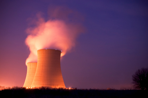 Nuclear Power Plant Cooling Towers at with stream pouring out into the purple blue dusk night sky