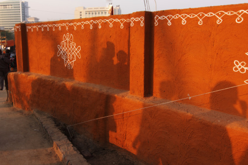Ethnic adobe mud wall painted in orange Color and decorated with Old style village art work in white paint.