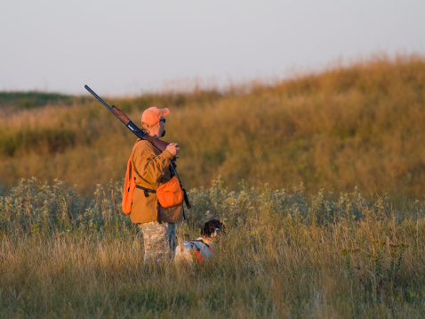 A hunter out on the prairie in the early morning sun with his dog