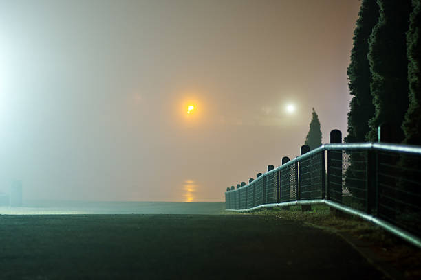 ogrodzenie przez rzekę w foggy nocy - street light fog morning country road zdjęcia i obrazy z banku zdjęć