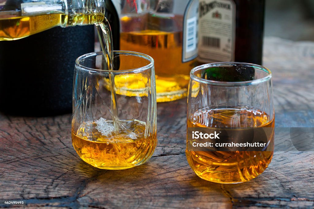 Two glasses with whiskey pouring in over a wooden table Golden Brown Whisky on the rocks in a glass Rum Stock Photo
