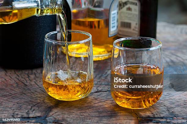Two Glasses With Whiskey Pouring In Over A Wooden Table Stock Photo - Download Image Now