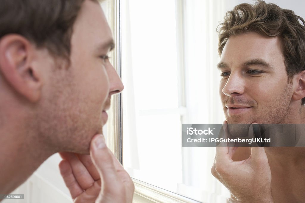 Man Examining His Stubble In Mirror Closeup of a young man examining his stubble in mirror Adult Stock Photo