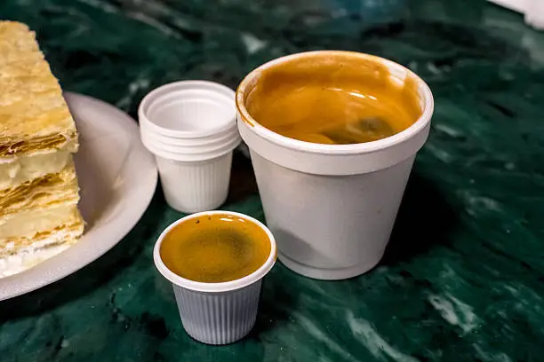 A cub of Cuban Coffee with the small "shot" cups used for dosing.  In the background a Cuban cream filled dessert is seen.