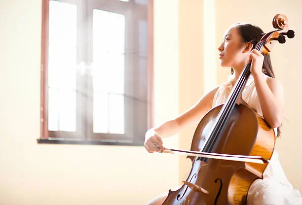 East asian teenage girl playing cello indoor,sunlight shining from the window