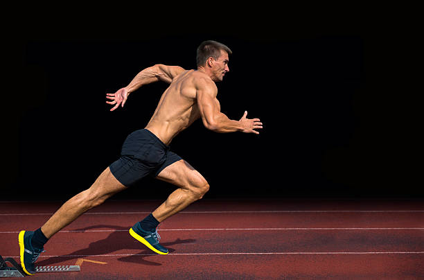 Off the Blocks, Athlete Practicing Start on 100m Sprint Side view of young adult athlete practicing start on 100 m, black background, real athlete human muscle photos stock pictures, royalty-free photos & images
