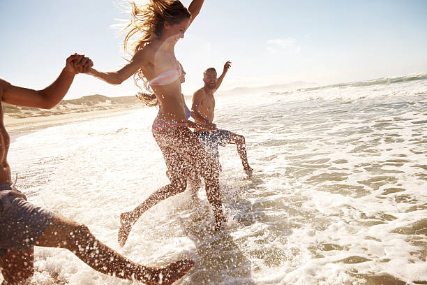 Splashing through the waves Two young couples running through the water at the beach beach fun stock pictures, royalty-free photos & images