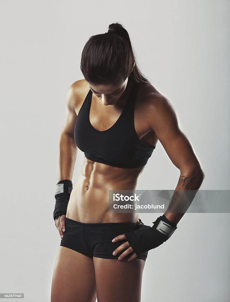 Fitness female resting after workout Muscular young woman athlete standing looking down with her hands on hips on grey background. Woman bodybuilder relaxing after exercise. 20-24 Years Stock Photo