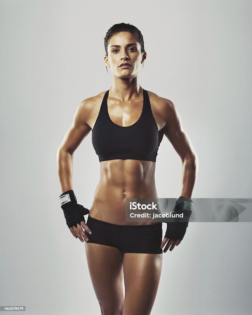 Fit and sexy young woman posing in grey background Portrait of sexy young woman with her hands on hips looking at camera. Fitness female with muscular body ready wearing hand gloves for workout on grey background Exercising Stock Photo